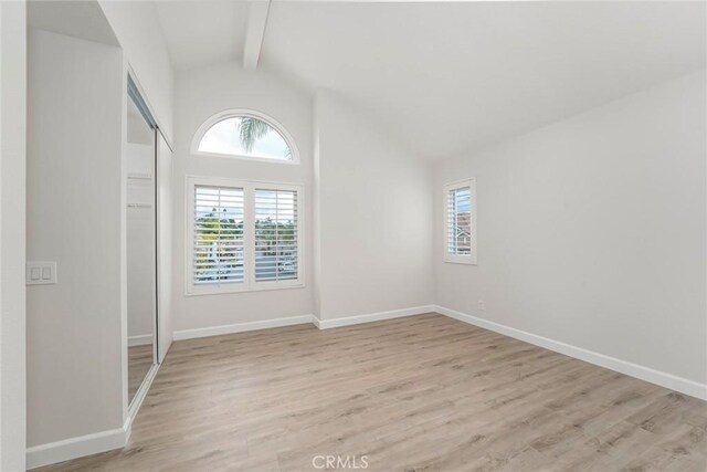 unfurnished room featuring plenty of natural light, light hardwood / wood-style flooring, and vaulted ceiling with beams