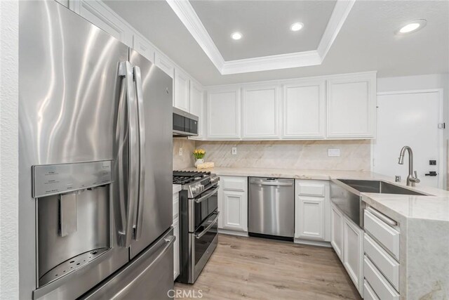 kitchen featuring appliances with stainless steel finishes, white cabinetry, a tray ceiling, crown molding, and light hardwood / wood-style flooring