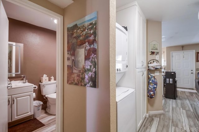 bathroom featuring toilet, vanity, wood finished floors, and stacked washer and clothes dryer