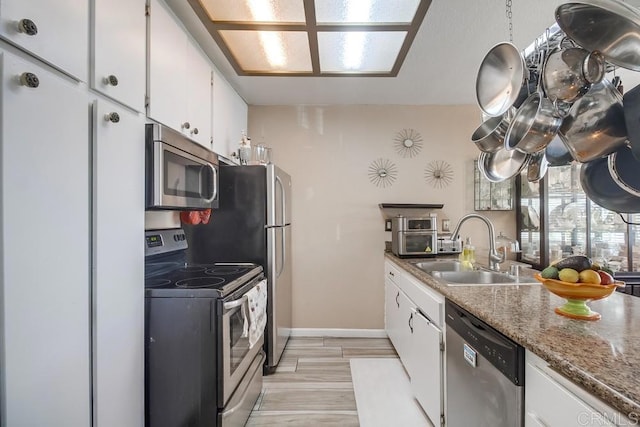 kitchen with stainless steel appliances, white cabinetry, a sink, and baseboards