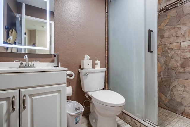 bathroom featuring a textured wall, a stall shower, vanity, and toilet