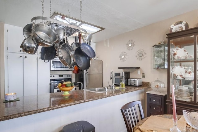 kitchen with appliances with stainless steel finishes, dark stone countertops, and a sink