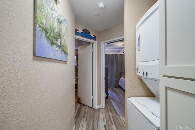 laundry room with wood finish floors, stacked washer and clothes dryer, laundry area, and a textured wall