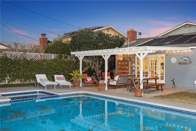 pool at dusk with a pergola and a patio area