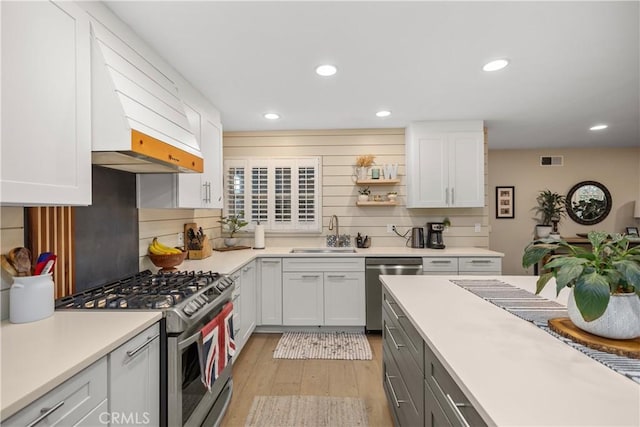 kitchen with custom range hood, stainless steel appliances, white cabinetry, and sink