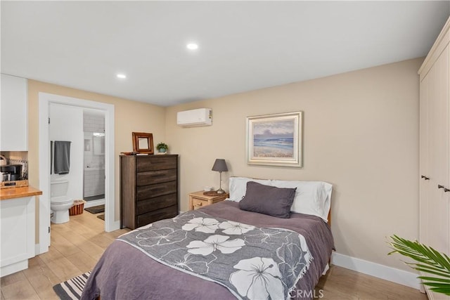 bedroom with a wall mounted AC, a closet, connected bathroom, and light hardwood / wood-style floors