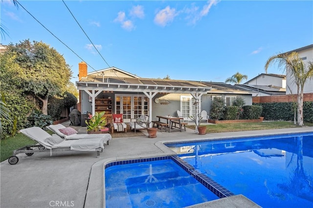 rear view of property with an outdoor structure, a fenced in pool, french doors, and a patio