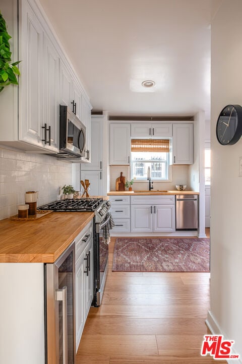 kitchen with white cabinetry, butcher block countertops, appliances with stainless steel finishes, light wood-type flooring, and sink