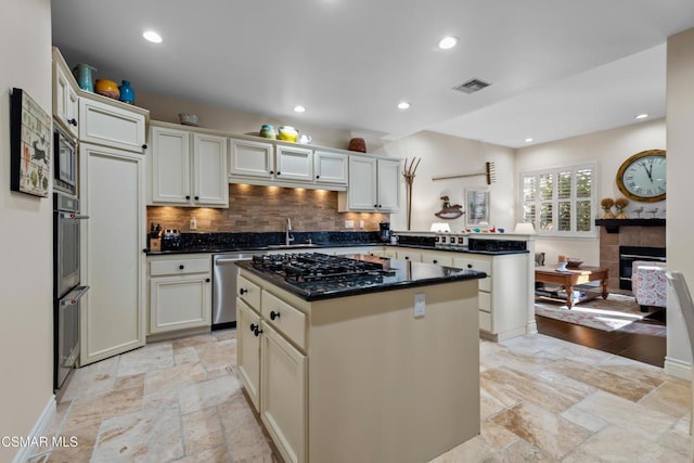 kitchen featuring a tile fireplace, decorative backsplash, a center island, kitchen peninsula, and stainless steel appliances