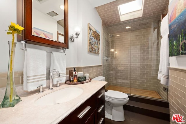 bathroom with toilet, tile walls, a shower with door, and vanity