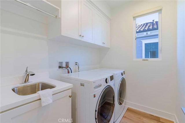 laundry area featuring cabinets, light hardwood / wood-style floors, washer and clothes dryer, and sink