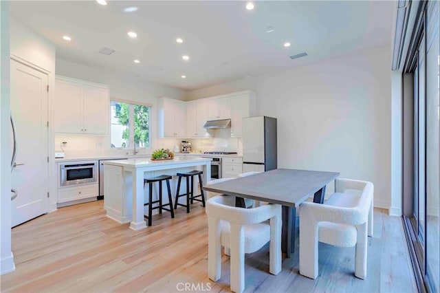 kitchen featuring white cabinetry, light hardwood / wood-style floors, white refrigerator, stainless steel stove, and a center island