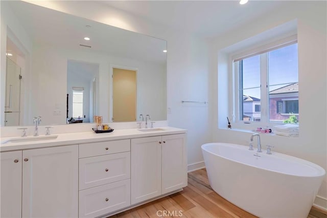 bathroom with a tub to relax in, vanity, and wood-type flooring