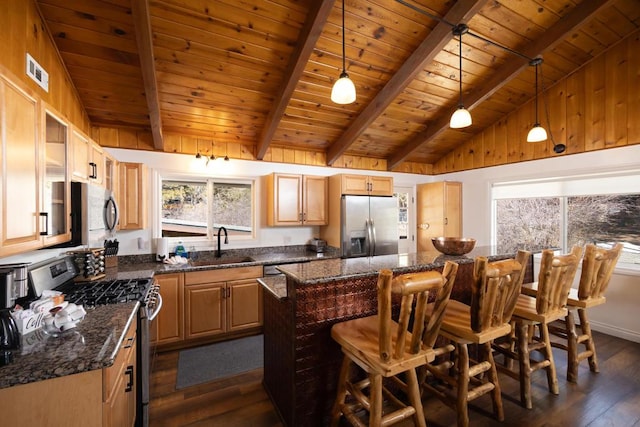 kitchen featuring appliances with stainless steel finishes, beam ceiling, dark stone counters, and decorative light fixtures