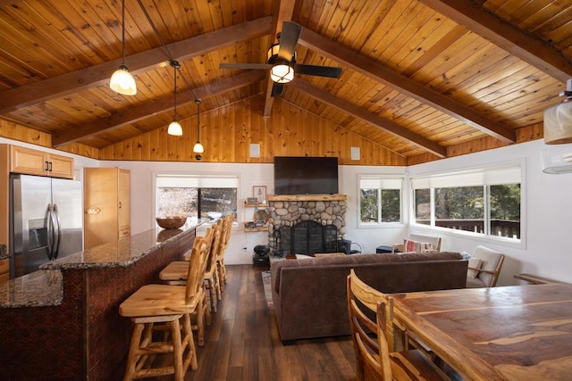 living room with wood ceiling, dark wood-type flooring, a stone fireplace, beamed ceiling, and ceiling fan