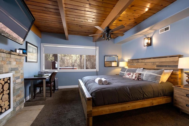 bedroom with a stone fireplace, beamed ceiling, dark colored carpet, ceiling fan, and wooden ceiling