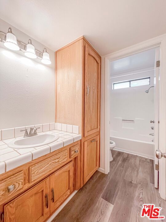 full bathroom featuring toilet, hardwood / wood-style flooring, vanity, and washtub / shower combination