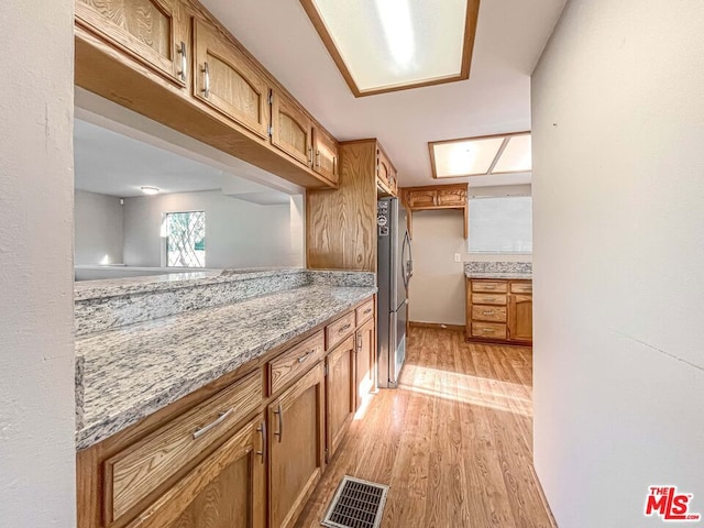 kitchen featuring light wood-type flooring, stainless steel refrigerator, and light stone counters