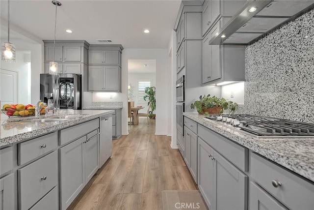 kitchen with light stone countertops, pendant lighting, appliances with stainless steel finishes, wall chimney exhaust hood, and gray cabinets