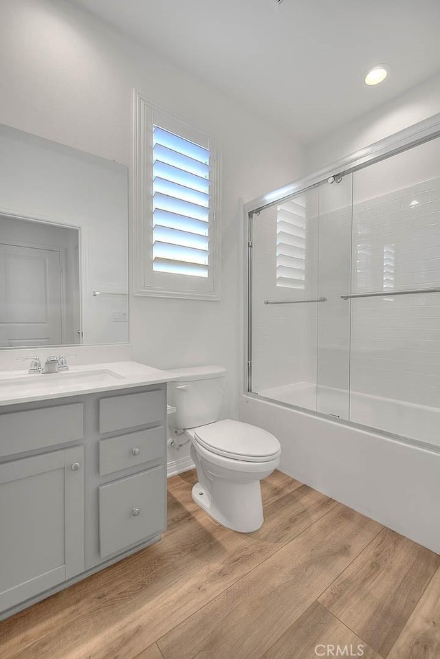 full bathroom with hardwood / wood-style flooring, shower / bath combination with glass door, vanity, and toilet