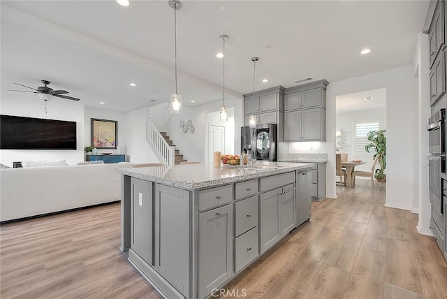 kitchen featuring hanging light fixtures, light wood-type flooring, light stone counters, a center island with sink, and gray cabinets