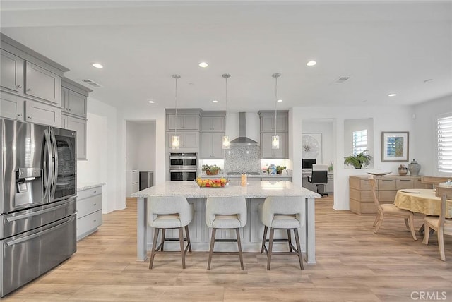 kitchen featuring hanging light fixtures, a kitchen island with sink, decorative backsplash, wall chimney range hood, and stainless steel appliances