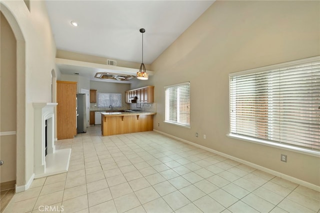 kitchen with tasteful backsplash, kitchen peninsula, hanging light fixtures, light tile patterned floors, and stainless steel fridge