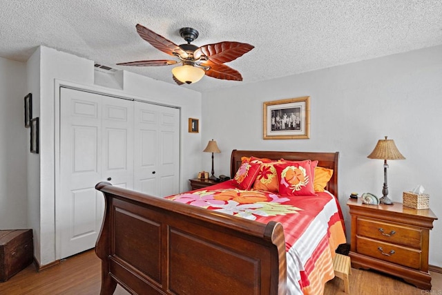 bedroom with a textured ceiling, light hardwood / wood-style floors, a closet, and ceiling fan