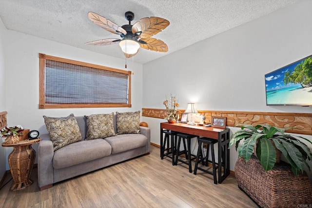 living room featuring ceiling fan, light hardwood / wood-style flooring, and a textured ceiling