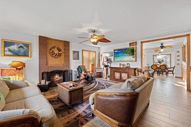 living room with a brick fireplace, ceiling fan, and light hardwood / wood-style flooring