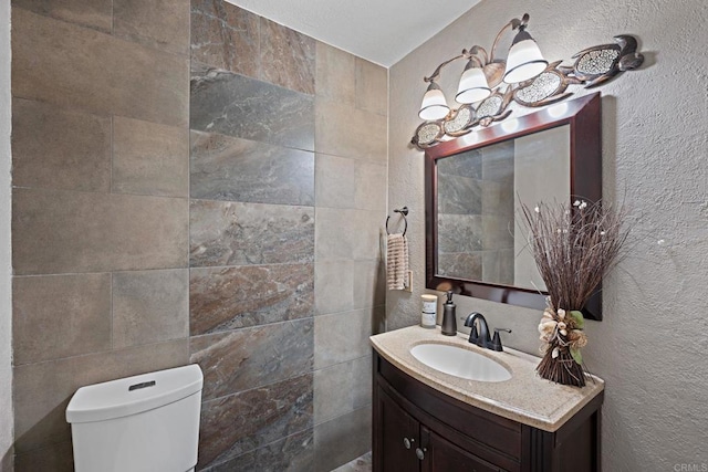 half bathroom featuring toilet, vanity, and a textured wall