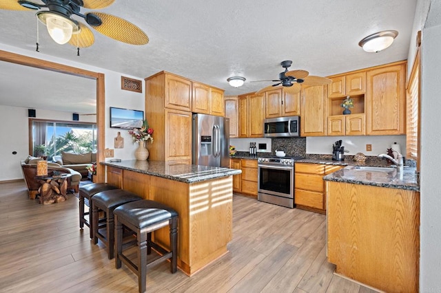 kitchen with a sink, a kitchen breakfast bar, light wood-style floors, and appliances with stainless steel finishes