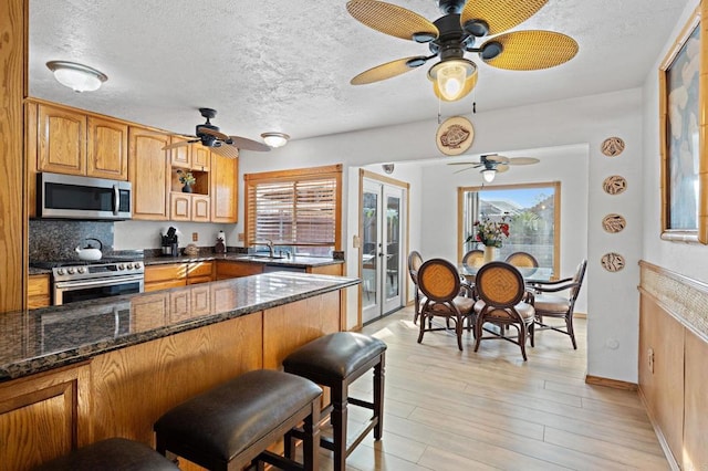 kitchen featuring dark stone countertops, appliances with stainless steel finishes, light wood-type flooring, and a kitchen breakfast bar