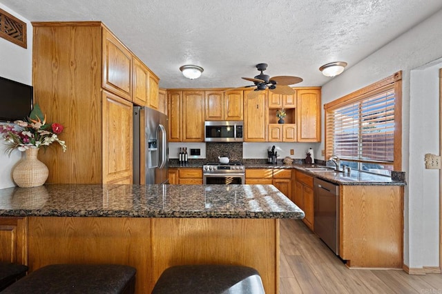 kitchen featuring a peninsula, ceiling fan, a sink, appliances with stainless steel finishes, and light wood-type flooring