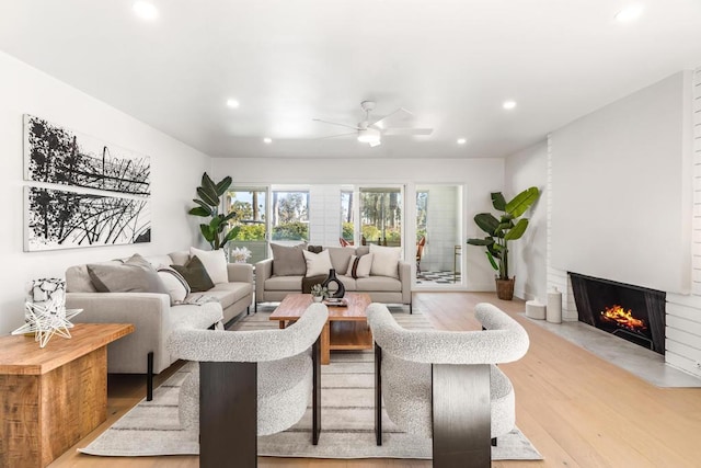 living room featuring ceiling fan, a large fireplace, and light hardwood / wood-style floors