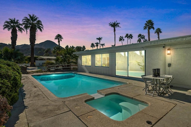 pool at dusk featuring a patio area, a mountain view, and an in ground hot tub