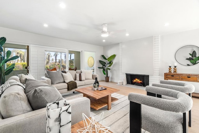 living room with ceiling fan, a large fireplace, and light hardwood / wood-style flooring