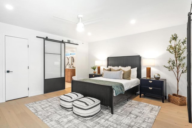 bedroom with ceiling fan, a barn door, ensuite bathroom, and light hardwood / wood-style flooring