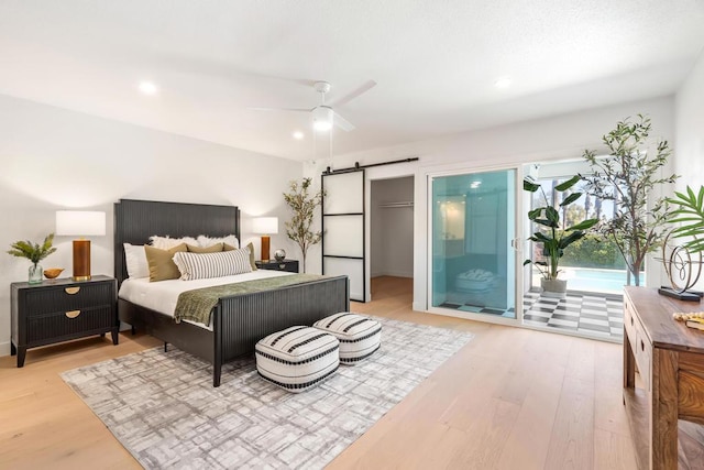 bedroom with ceiling fan, a barn door, access to exterior, light hardwood / wood-style flooring, and a closet