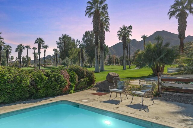 pool at dusk with a mountain view, a yard, and a patio