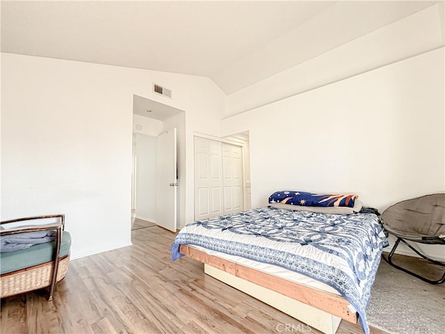 bedroom with lofted ceiling, light hardwood / wood-style flooring, and a closet