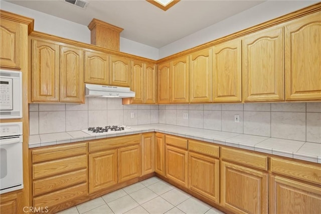 kitchen with light tile patterned flooring, tile countertops, backsplash, and white appliances