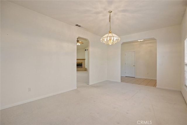 carpeted spare room featuring ceiling fan with notable chandelier