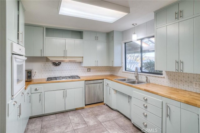 kitchen with appliances with stainless steel finishes, decorative backsplash, sink, hanging light fixtures, and butcher block countertops