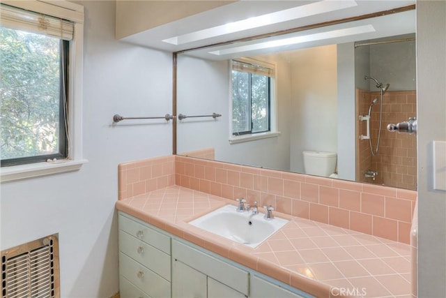 bathroom with vanity, decorative backsplash, toilet, heating unit, and a tile shower