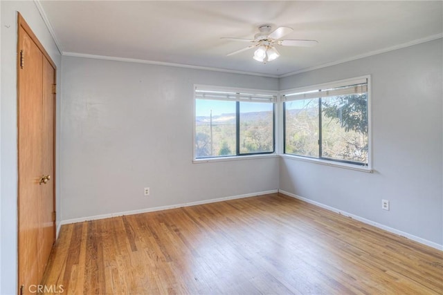 spare room with ornamental molding, light wood-style floors, baseboards, and ceiling fan