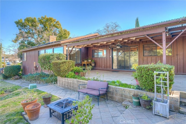 back of house with a patio, a chimney, board and batten siding, ceiling fan, and a fire pit