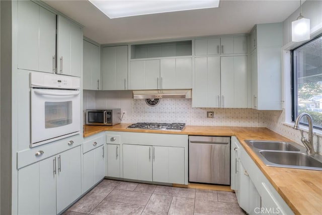 kitchen with appliances with stainless steel finishes, butcher block counters, pendant lighting, and sink