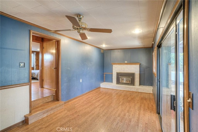 unfurnished living room featuring a ceiling fan, a brick fireplace, crown molding, and light wood-style flooring