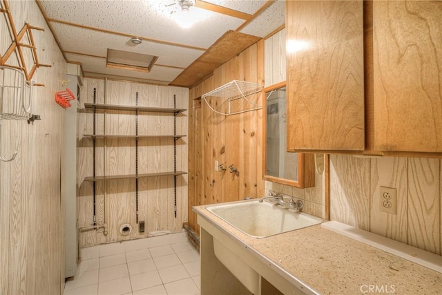 laundry room with light tile patterned floors, attic access, wooden walls, and a sink